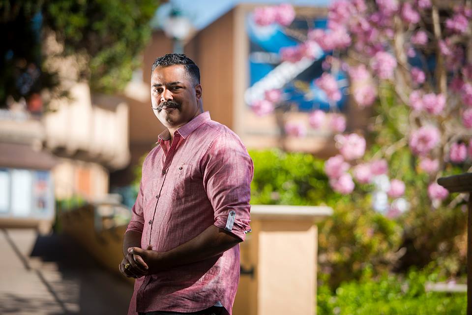 Freedome Bradley-Ballentine outdoors in Balboa Park, blossoms behind him